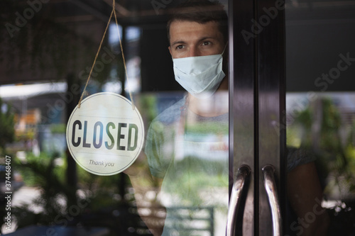 Chef in safety mask hanging up sign closed on restaurant door. photo