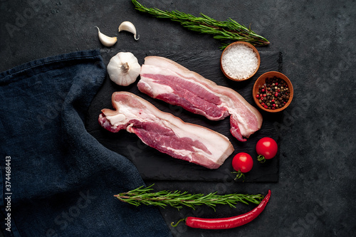 raw pork breast with spices on a slate board on a stone background