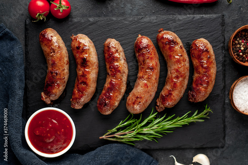 grilled sausages with spices on a slate board on a stone background