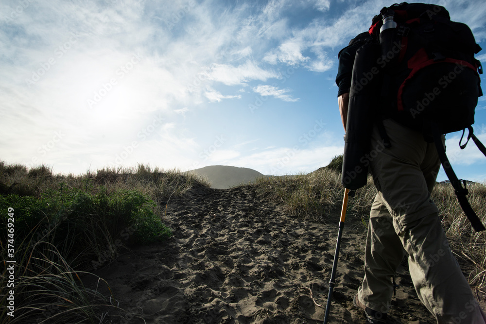 A backpacker walking on the sand track towards the Anawhata beach, Auckland