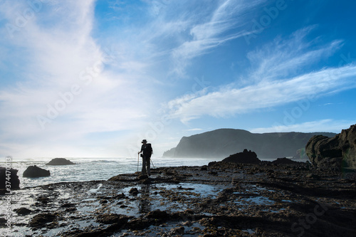 A backpacker standing on the rocks at Anawhata beach, Waitakere, Auckland