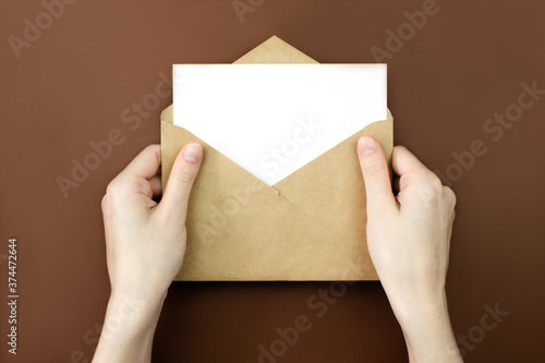 Envelope and white empty letter mock-up in female hands top view with copy space. Communication, information, post, mail concept. Web, social media banner template. Stock photo.