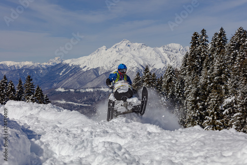 Pro snowmobiler makes a turn and lets a flurry of snow spray from under the caterpillar. sports snowmobile in the mountains. bright skidoo motorbike and suit without brands. Winter fun moto extreme