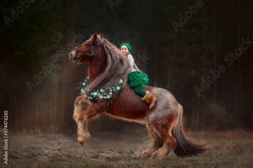Little girl in green dresshorseback on red tinker horse in christmas wreath © Julia Shepeleva