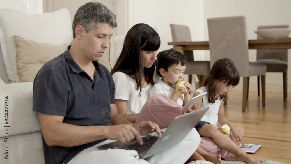 Focused parents couple using computers while children sitting near them and eating fresh apples in apartment. Communication and parenthood concept Focused parents couple using computers while children sitting near them and eating fresh apples in apartment. Communication and parenthood concept
