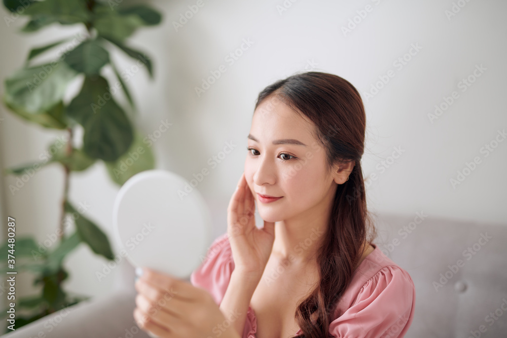 Young Asian woman holding and looking in the mirror at living room Young Asian woman holding and looking in the mirror at living room