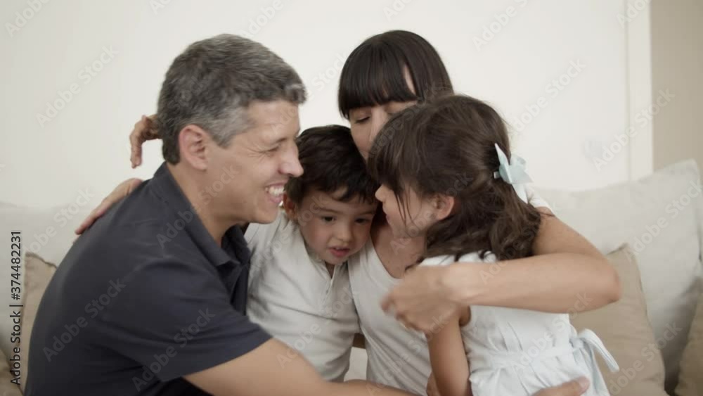 Happy joyful parents couple and two cute little kids sitting on couch in apartment, hugging each other, enjoying leisure time together. Medium shot. Family leisure time concept Happy joyful parents couple and two cute little kids sitting on couch in apartment, hugging each other, enjoying leisure time together. Medium shot. Family leisure time concept