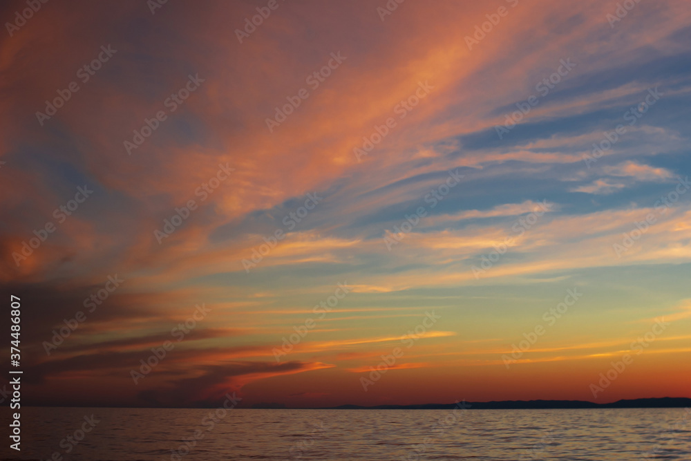 Dramatic clouds on the blue sky in pink yellow red shades in the sunset light on Lake Baikal, beautiful scenic seascape