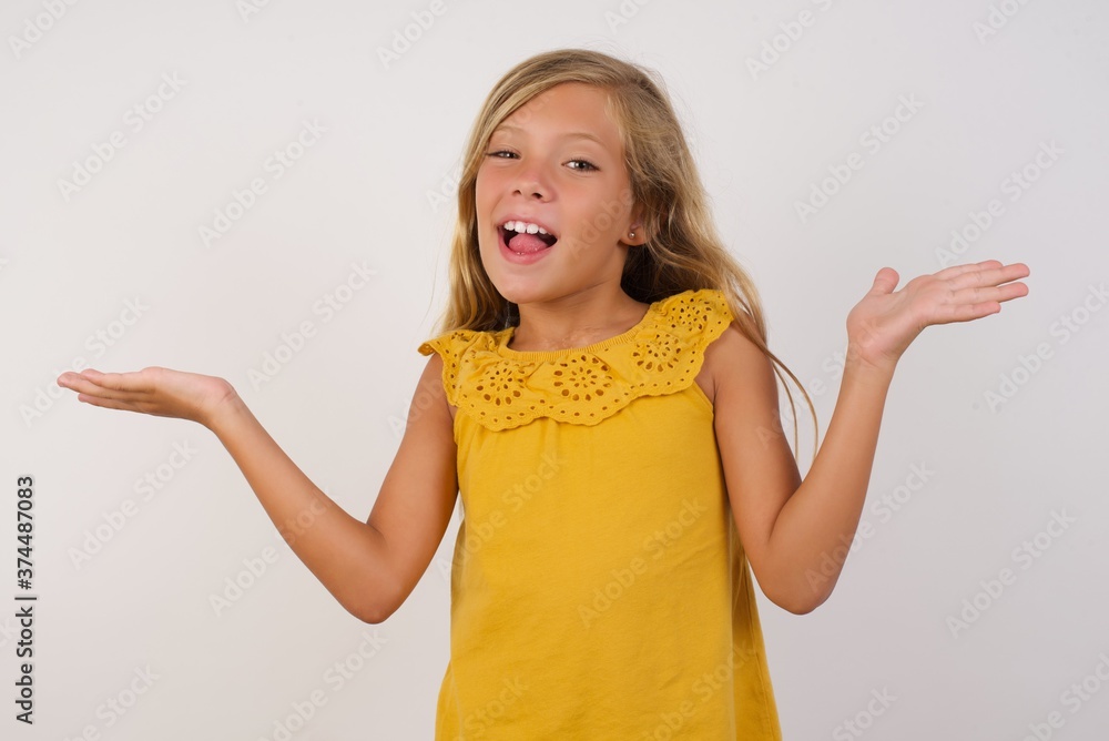 Little blond girl wearing yellow dress over white background celebrating crazy and amazed for success with arms raised and open eyes screaming excited. Winner concept Little blond girl wearing yellow dress over white background celebrating crazy and amazed for success with arms raised and open eyes screaming excited. Winner concept
