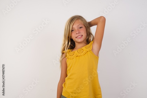 Young blonde kid girl wearing yellow dress over white background confuse and wonder about question. Uncertain with doubt, thinking with hand on head. Pensive concept.