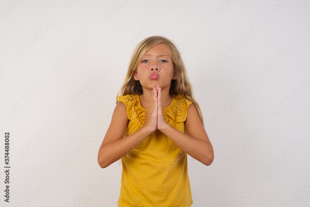 Positive adorable Little girl with beautiful blonde hair over white background smiles happily, glad to receive pleasant news from interlocutor, keeps palms together, People emotions concept. Positive adorable Little girl with beautiful blonde hair over white background smiles happily, glad to receive pleasant news from interlocutor, keeps palms together, People emotions concept.