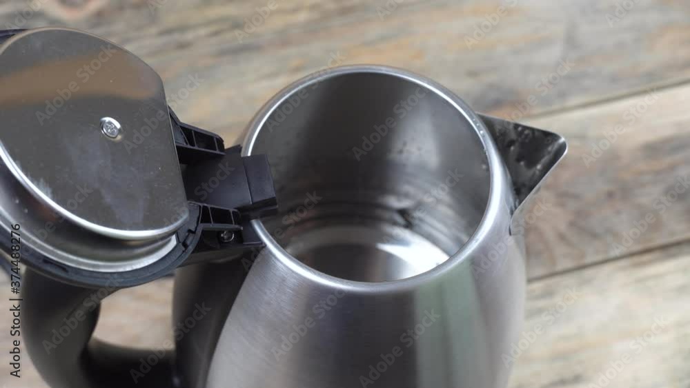 Water is poured into a shiny metal kettle. on a wooden background. Close-up. View from above. Water is poured into a shiny metal kettle. on a wooden background. Close-up. View from above.