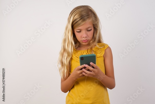 Portrait of excited Little girl with beautiful blonde hair over white background  winking and eye hold smart phone use read social network news