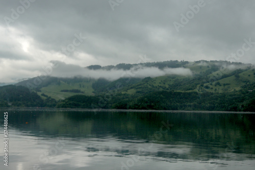 Mountains and hills reflecting in the clear water of lake - hazy clouds on the sky