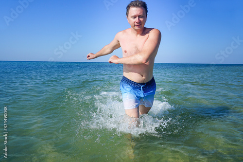 The guy runs along the waves in the sea with azure water. Splashes fly to the sides