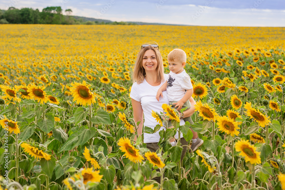 little boy with mom in a white t-shirt walks in a field of sunflowers little boy with mom in a white t-shirt walks in a field of sunflowers