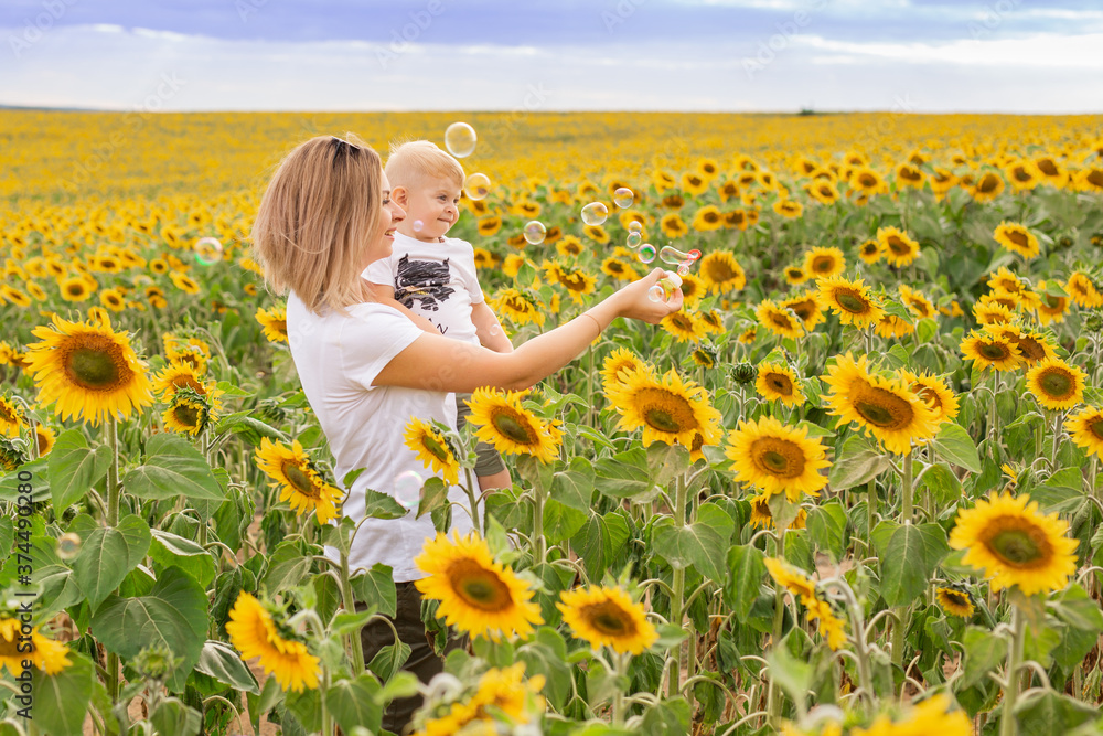 little boy with mom in a white t-shirt walks in a field of sunflowers little boy with mom in a white t-shirt walks in a field of sunflowers