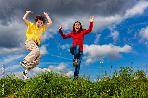 Girl and boy running, jumping against blue sky 