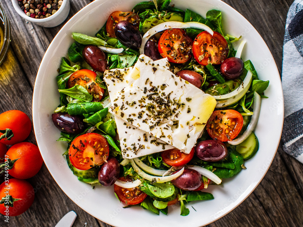 Fresh Greek salad - feta cheese, tomatoes, cucumber, red pepper, black olives and onion on wooden table Fresh Greek salad - feta cheese, tomatoes, cucumber, red pepper, black olives and onion on wooden table