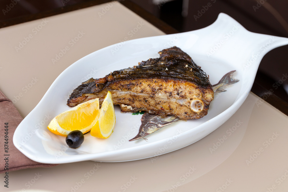 Fried fish flounder with lemon and black olives on a white plate Fried fish flounder with lemon and black olives on a white plate