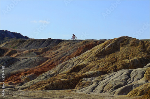 Mounds in a clay quarry. In the distance, the silhouette of a lone cyclist against the sky. Cyclist in the mountains.