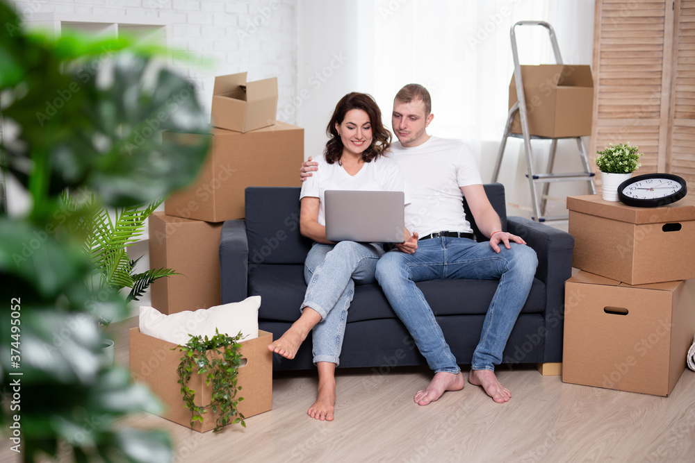 happy young couple looking something in laptop surrounded by cardboard boxes happy young couple looking something in laptop surrounded by cardboard boxes