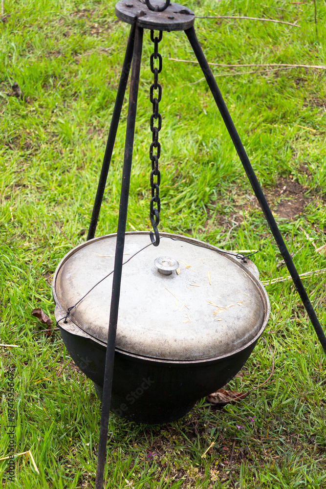 Cauldron for cooking in a hike against a background of green grass. Active tourism. Cauldron for cooking in a hike against a background of green grass. Active tourism.
