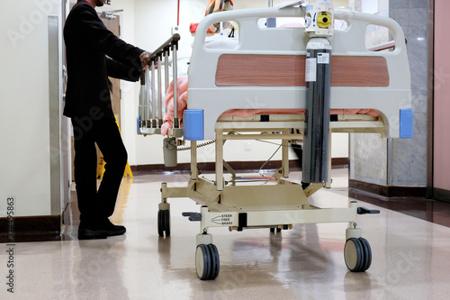 A patient on a hospital stretcher bed waits by the elevator as he is being transported from the ward for medical treatment by a medical concierge attendant or assistant at a private hospital. photo