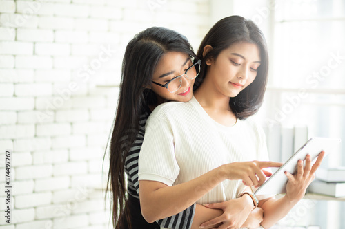 Young Attractive Asian lesbian couple hugging and working at home together with smart tablet. Asian women new normal and happy life. LGBT concept.