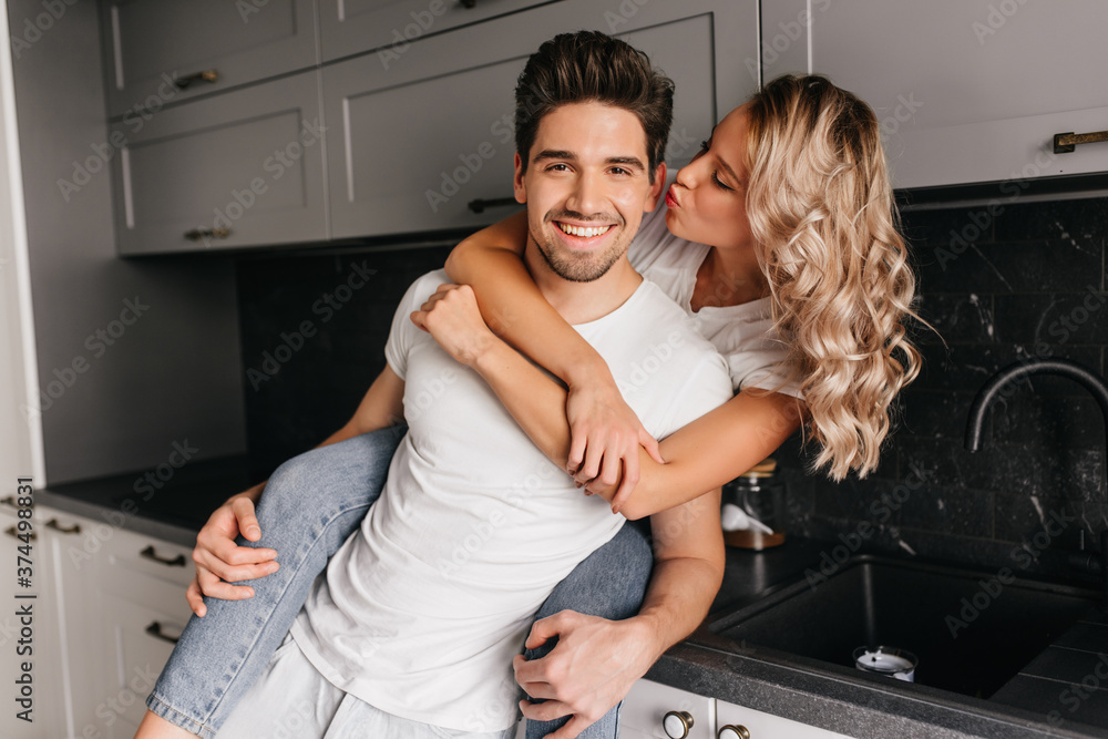 Charming curly girl kissing boyfriend. Amazing fair-haired young woman embracing husband. Charming curly girl kissing boyfriend. Amazing fair-haired young woman embracing husband.