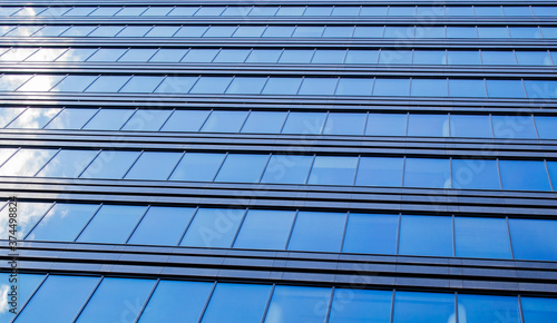 Endless rows of identical gray Windows of a modern glass office building-a skyscraper which reflects the blue sky and white clouds