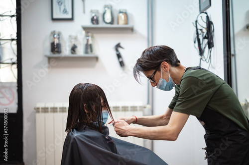 Hairdresser and girl child customer in a salon with medical masks during virus pandemic. Working with safety mask.