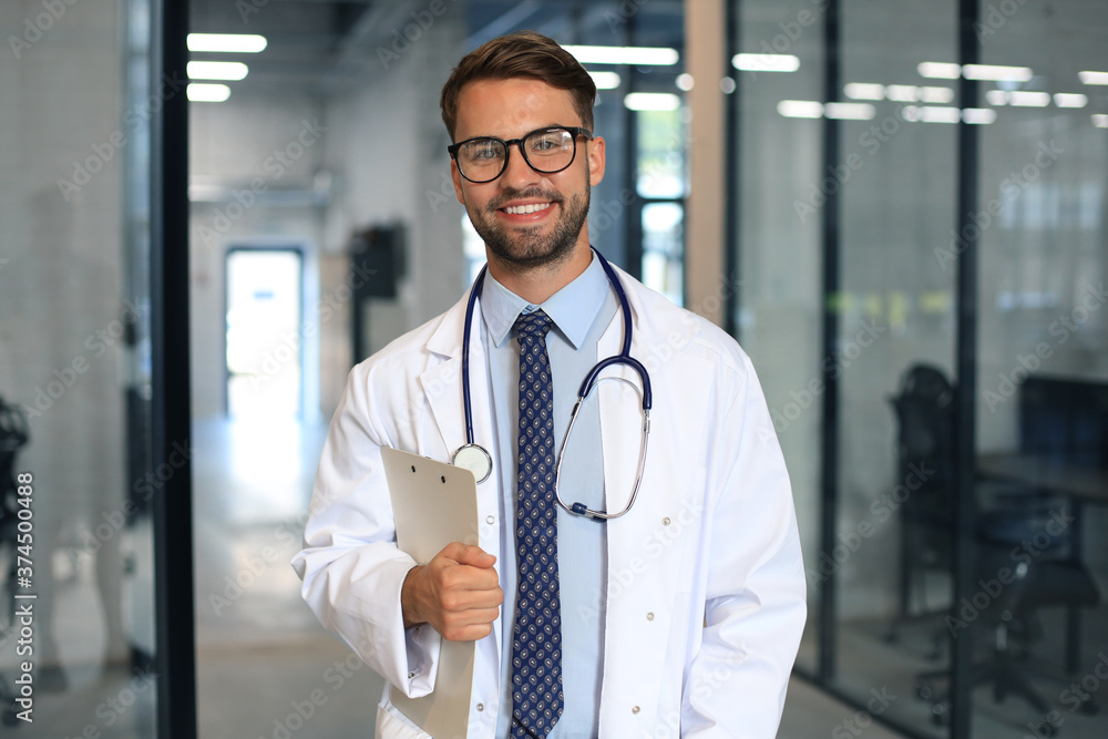 Handsome friendly young doctor on hospital corridor looking at camera, smiling. Handsome friendly young doctor on hospital corridor looking at camera, smiling.