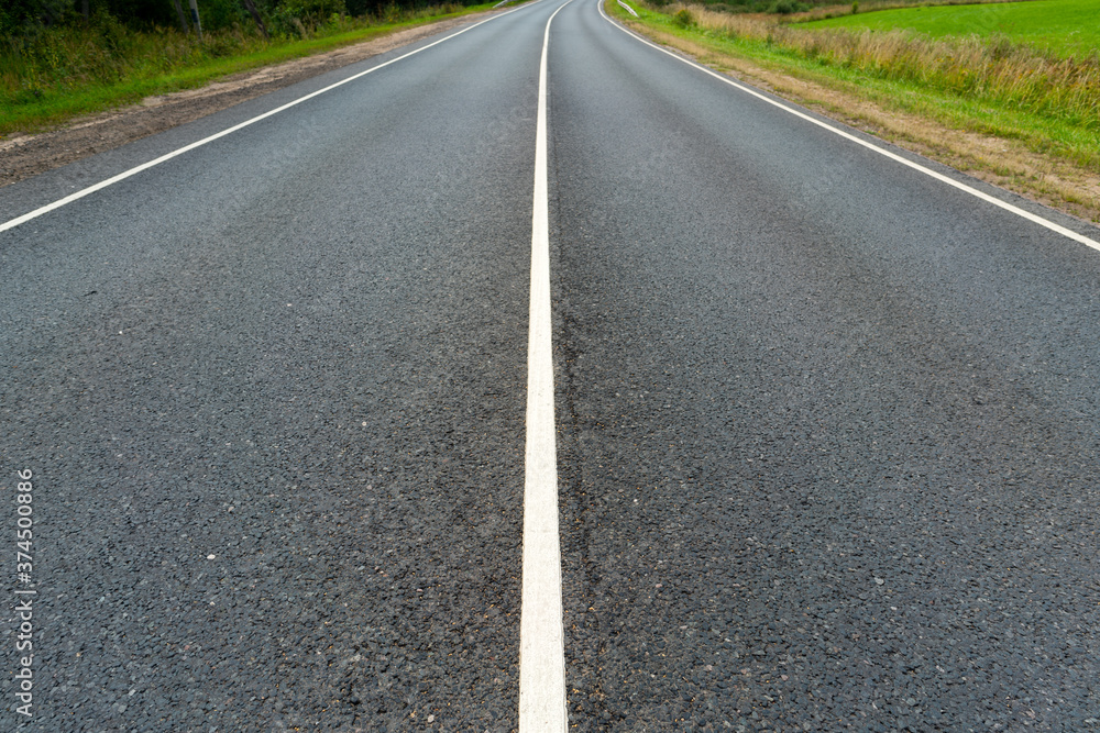 The dividing strip of an asphalt country road. White road markings.