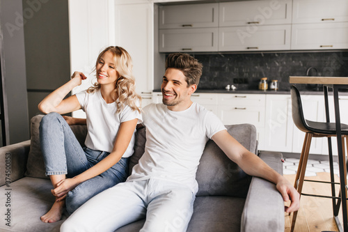 Smiling couple sitting on sofa in modern apartaments and watching tv. Joyful young man with his beautiful girlfriend relaxing at home.