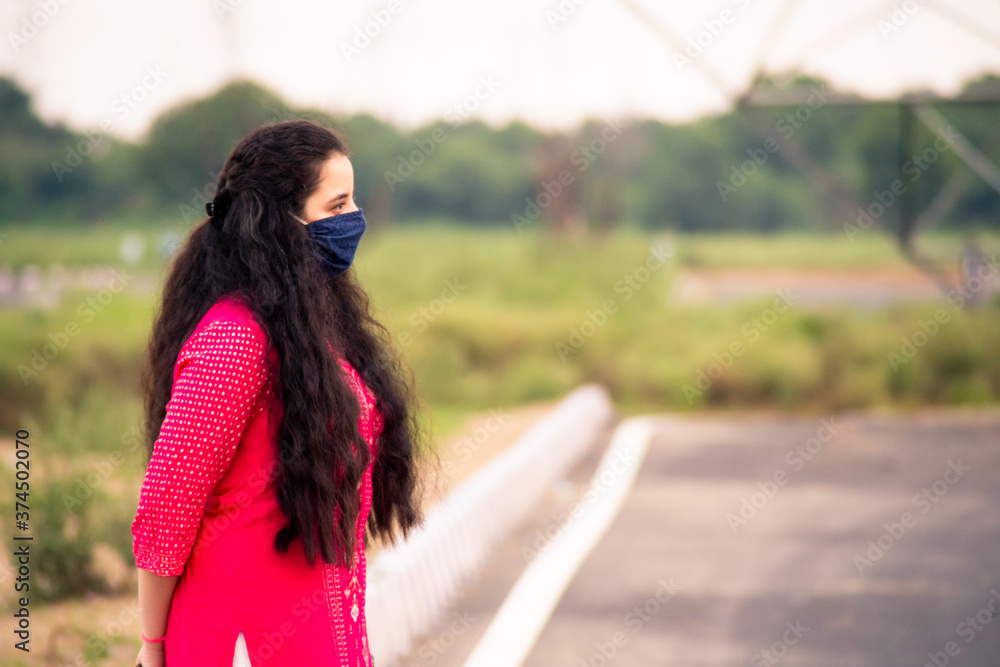 Young Indian girl wearing a mask, indian salwar kameez standing with a field and a beautiful sunset behind her