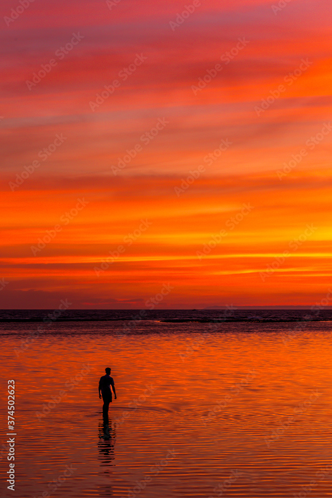 Person silhouetted walking in the water at sunset