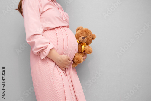 Close up of pregnant woman belly with teddy bear toy. Pregnancy, parenting, preparation and expectation concept..