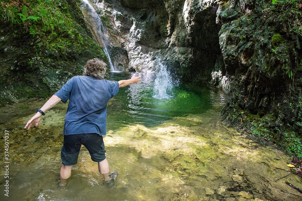 An adult hiker on an adventurous hike through the Gačnik canyon throws stones into the water, Soca valley, Slovenia, Europe An adult hiker on an adventurous hike through the Gačnik canyon throws stones into the water, Soca valley, Slovenia, Europe