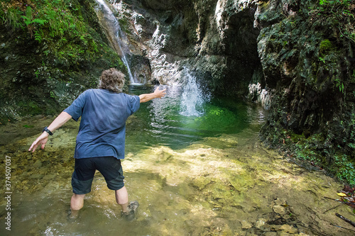 An adult hiker on an adventurous hike through the Gačnik canyon throws stones into the water, Soca valley, Slovenia, Europe