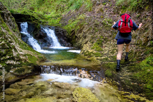 Adult hiker with a backpack on an adventurous hike through the canyon of the river Gačnik, Soca valley, Slovenia, Europe. Majestic waterfalls in the background.