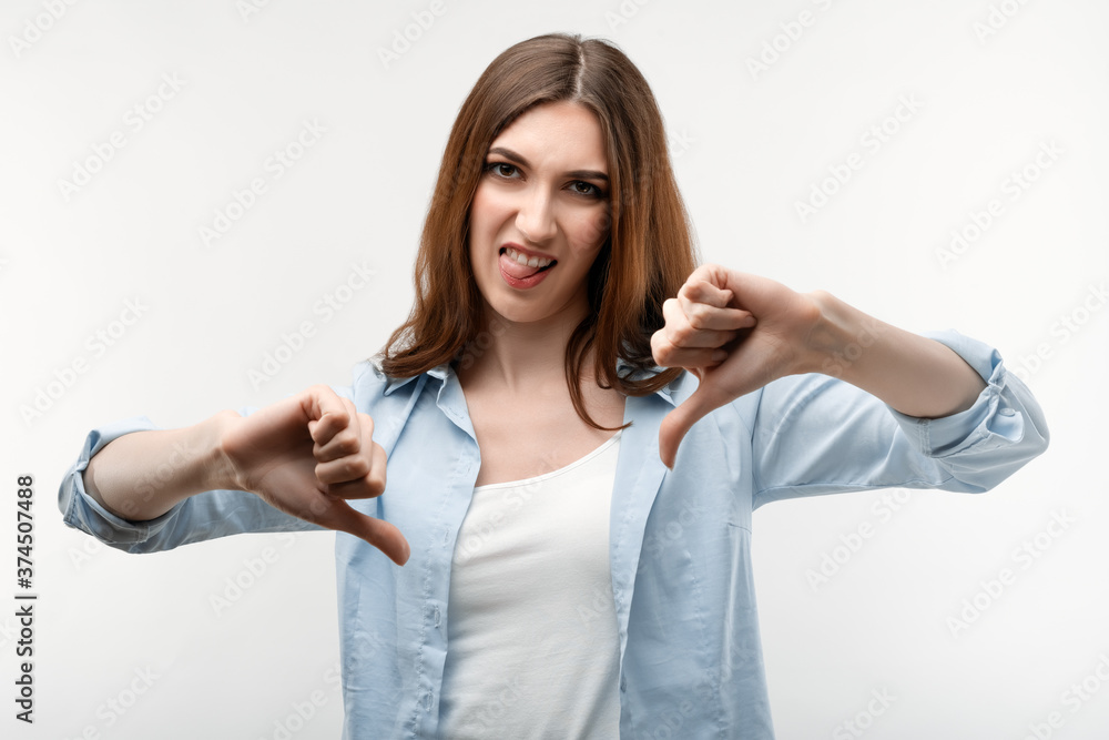 Beautiful girl with long chestnut hair holding two thumbs down. Concept of dislike. Beautiful girl with long chestnut hair holding two thumbs down. Concept of dislike.