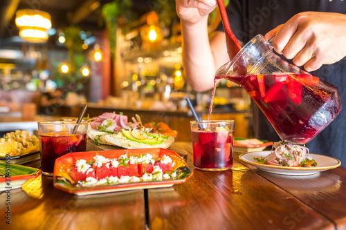 Bartender pouring a glass of red sangria with fresh fruit and tapas on the table at a restaurant