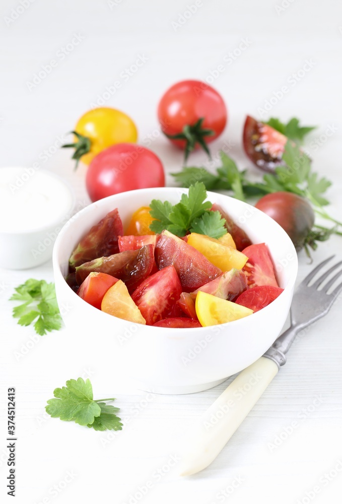 Vegetable salad of fresh yellow, red and black tomatoes with parsley in a bowl on a white background