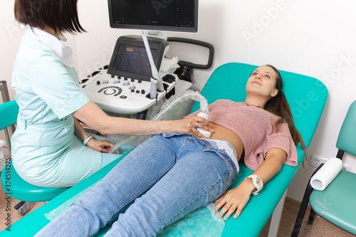 Doctor holds an ultrasound scanner in his hand and makes an ultrasound diagnosis of the abdominal cavity to the female patient. Medical research close up.