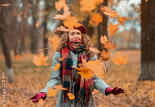 Closeup portrait of beautiful smiling girl holding autumn leaves in the park. Excited cheerful girl drop up leaves, joyful with beautiful autumn colors. Falling yellow leaves