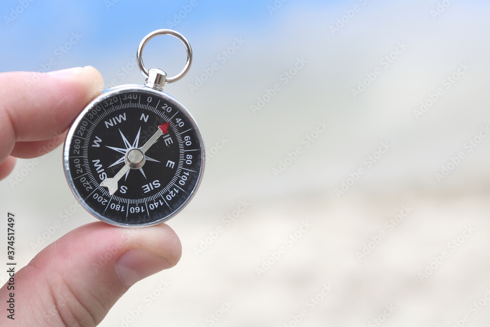 Classic compass in hand against background of sandy beach and blue sea as symbol of tourism with compass, travel with compass and outdoor activities with compass Classic compass in hand against background of sandy beach and blue sea as symbol of tourism with compass, travel with compass and outdoor activities with compass
