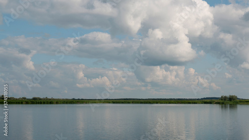 Forest lake view, smooth surface of a lake with clouds reflected, shining level of a forest lake