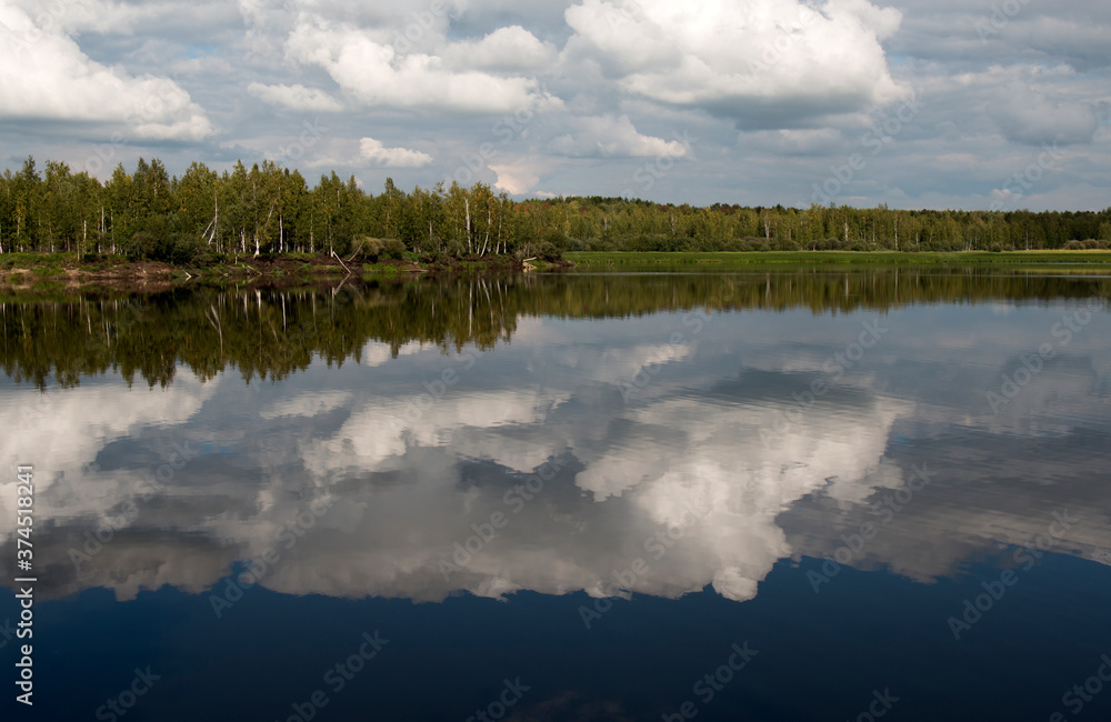 Fototapeta premium Forest lake view, smooth surface of a lake with clouds reflected, shining level of a forest lake