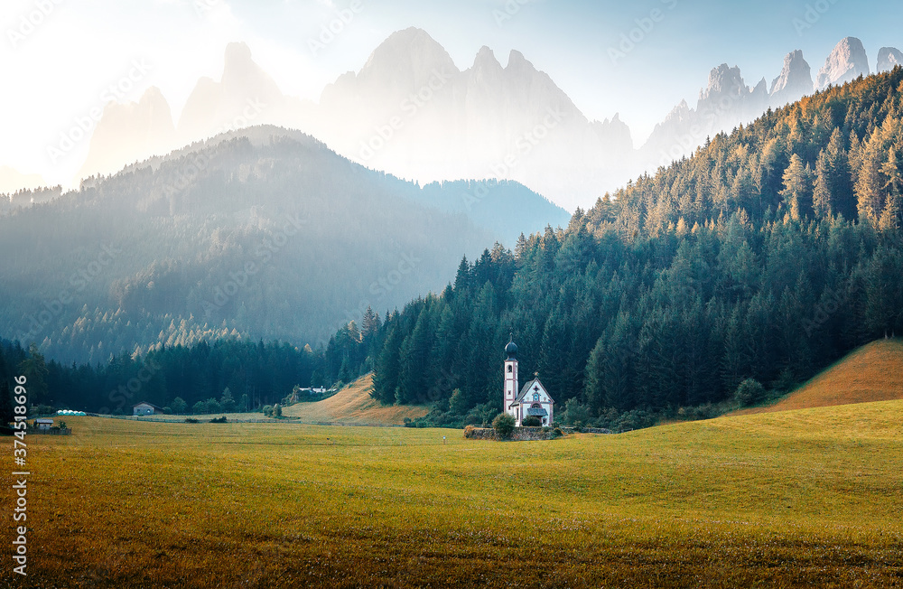 Incredible landscape with cloudy sky over the Dolomites mountains. Fantastic summer View on mountain valley with green grass under sunlight and famouse church in Santa Maddalena village in sunny day